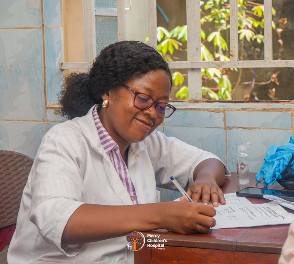 A paediatrician smiling while writing up notes at her desk
